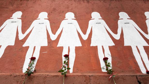 Eine rote Wand mit aufgemalten Frauenkörpern und roten Rosen davor