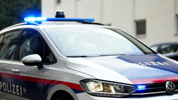 Ein silbernes Polizeiauto mit eingeschaltetem Blaulicht steht auf einer Straße vor einem Gebäude.