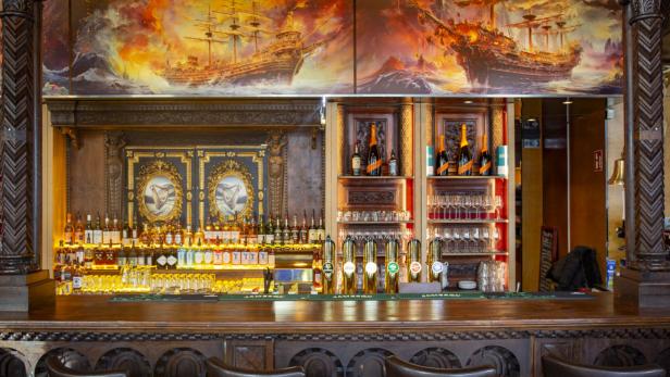 Eine Bar mit einer großen Auswahl an Spirituosen und einem Gemälde von Schiffen in stürmischer See.