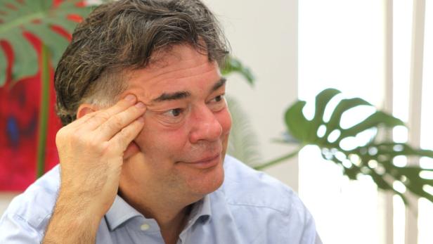 Ein Mann in einem hellblauen Hemd stützt sein Gesicht mit der Hand.