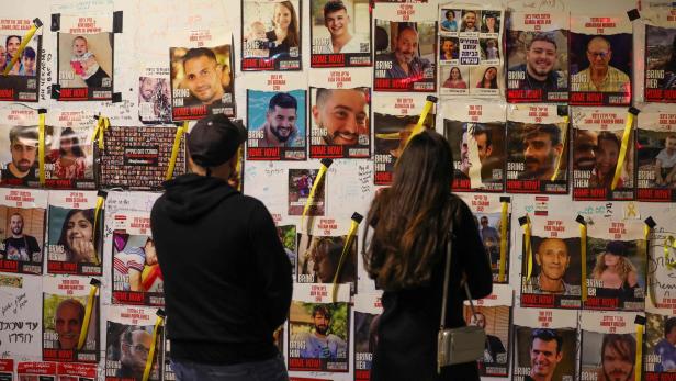 Zwei Passanten betrachten eine Wand mit Bildern der vielen Geiseln in Tel Aviv.