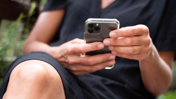 Person hält ein schwarzes Handy in den Händen.