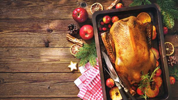 Ein gebratener Truthahn auf einem Backblech, umgeben von Äpfeln und Orangen.