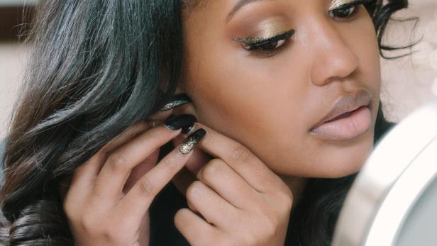 Eine Frau mit goldenem Make-up setzt sich einen Ohrring ein.