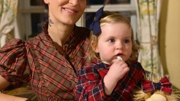 Eine Frau mit einem kleinen Mädchen auf dem Schoß, beide tragen karierte Kleider.