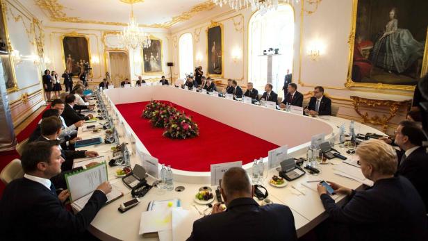 Ein formelles Treffen mit vielen Personen an einem langen Tisch in einem opulenten Raum.