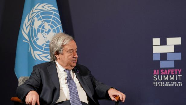 Antonio Guterres sitzt vor einer blauen Webewand, im Hintergrund ist die UNO-Fahne zu sehen.