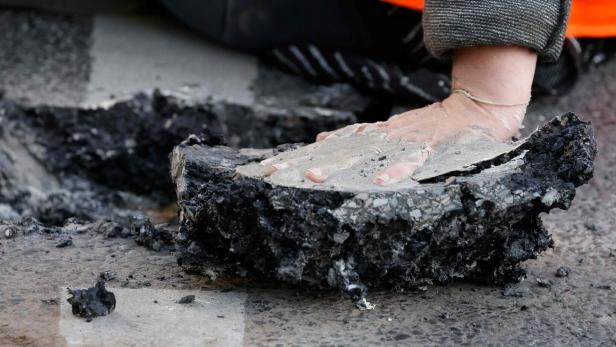 Eine Hand ist mit Beton auf einem Stück herausgebrochener Asphalt festgeklebt.