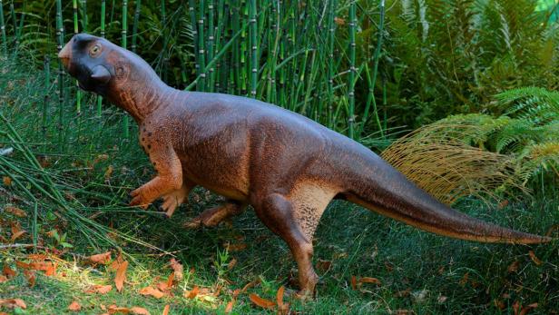 Ein brauner Dinosaurier steht in einer grünen, bewaldeten Umgebung.