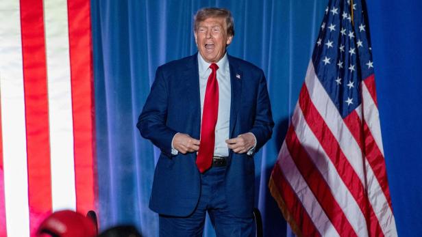 Donald Trump steht neben einer US-Fahn und schimpft