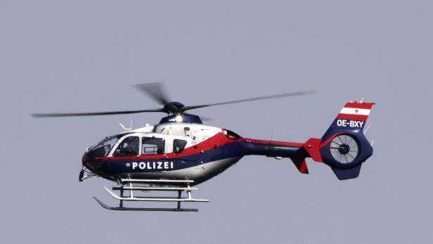 Ein rot-weiß-blauer Polizei-Hubschrauber fliegt am Himmel.
