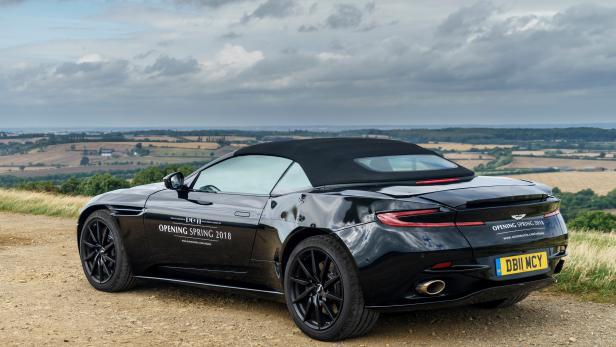 Ein schwarzer Aston Martin DB11 Volante steht auf einem Hügel mit Blick auf die Landschaft.