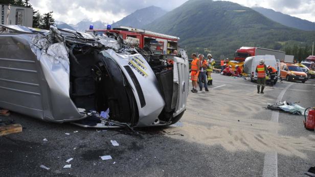 Ein schwerer Verkehrsunfall mit einem auf der Seite liegenden Kärcher-Transporter und Rettungskräften vor Bergkulisse.