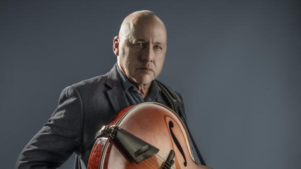 Ein Mann im Anzug hält eine Archtop-Gitarre.