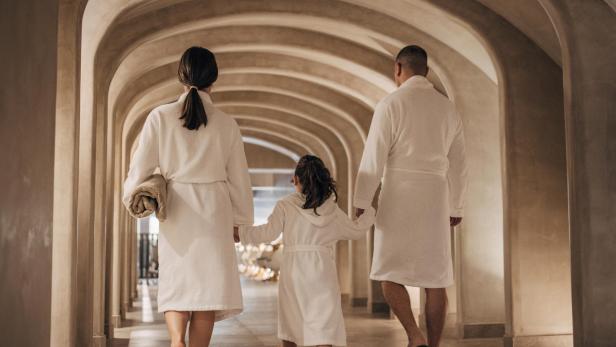 Eine Familie in Bademänteln geht in einem Wellnesshotel einen Flur entlang.