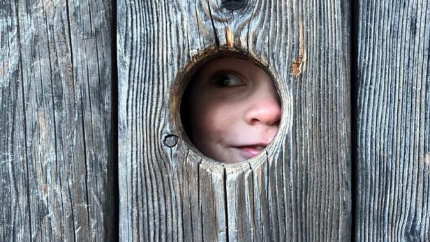 Kind schaut durch Guckloch in Holztüre