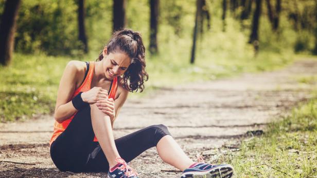 Eine Frau hält sich schmerzverzerrt das Knie beim Joggen.