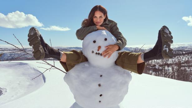 Eine Frau sitzt auf einem Schneemann in einer verschneiten Landschaft.