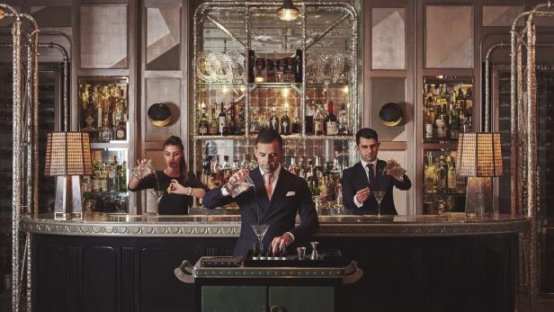 Drei Barkeeper bereiten in einer eleganten Bar Cocktails zu.