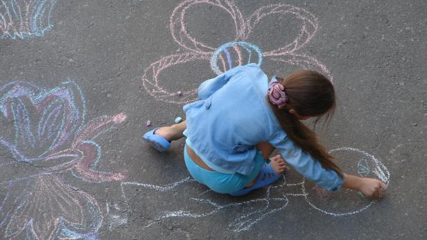 Ein Mädchen malt mit Kreide Blumen auf den Asphalt.