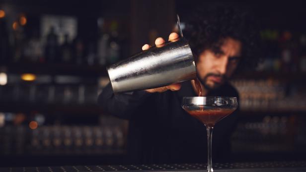 Ein Barkeeper gießt einen Cocktail aus einem Shaker in ein Glas.
