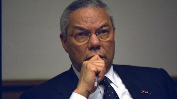 Colin Powell mit Brille und Anzug, nachdenklich mit einem Stift in der Hand.
