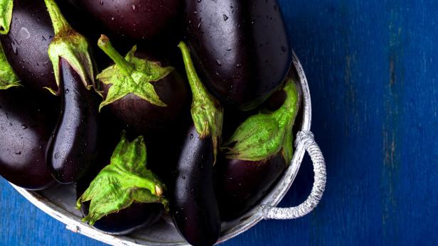 Fresh eggplant in grey basket on blue wooden table.Rustic background. Top view. Copy space. Vegan vegetable.