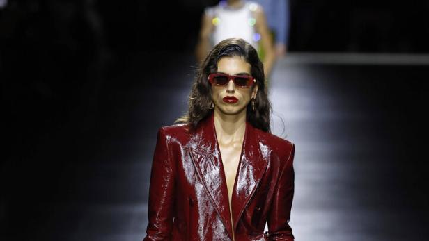 Eine Frau in einem roten Lacklederblazer und beigen Shorts auf einem Laufsteg.