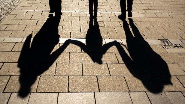 Die Schatten von drei Personen auf einem gepflasterten Weg.