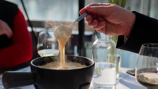 Eine Person hebt mit einem Löffel dampfendes Käsefondue aus einem Topf.