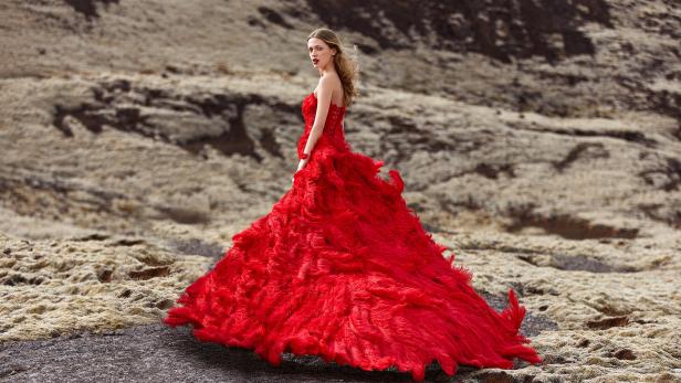 Eine Frau in einem roten Kleid steht in einer kargen Landschaft.