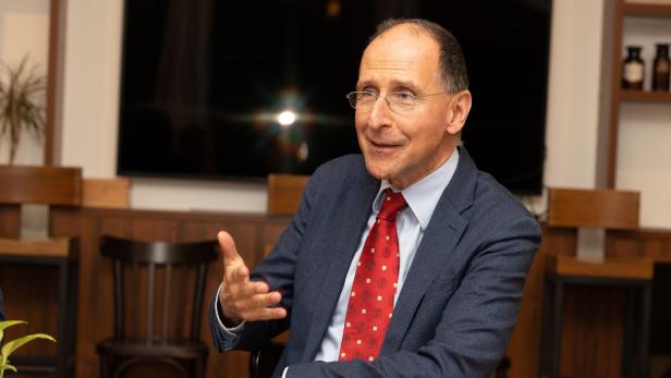 Ein Mann mit Brille, Anzug und roter Krawatte gestikuliert an einem Tisch.