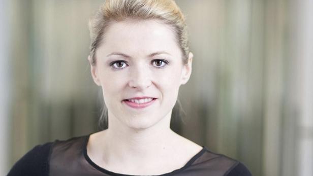 Porträt einer lächelnden Frau mit blonden Haaren und einem schwarzen Oberteil.