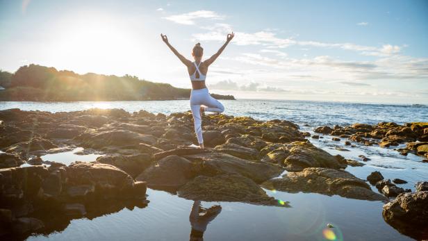 Eine Frau macht Yoga auf einem Felsen am Meer bei Sonnenaufgang.