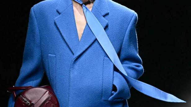 Ein Mann in einem blauen Mantel mit einer runden Gucci-Tasche auf dem Laufsteg.