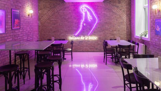 Ein Restaurant mit Tischen und Stühlen, beleuchtet mit violettem Neonlicht und dem Schriftzug „Italians do it better“.
