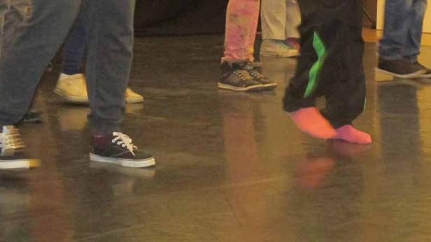 Mehrere Personen stehen barfuß oder mit Schuhen auf einem glänzenden Boden.