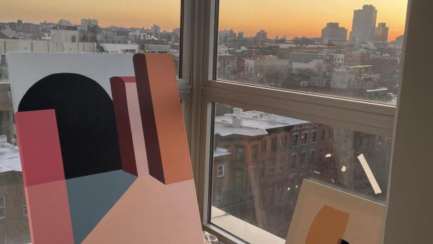 Gemälde in einem Artelier die vor einem Fenster mit dem Hintergrund der New Yorker Skyline stehen