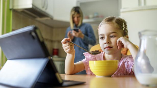 Mädchen schaut auf dem Tablet beim Frühstück essen