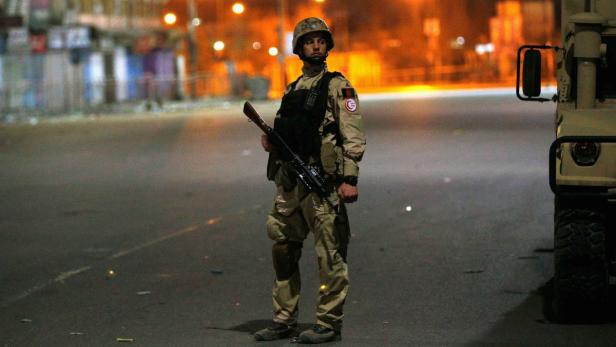 Ein Soldat steht nachts auf einer Straße mit einem Gewehr.