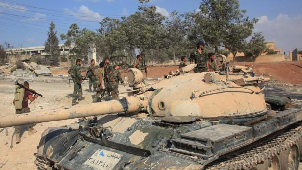 Soldaten stehen um einen Panzer in einer zerstörten städtischen Umgebung.