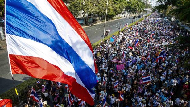 Eine große Menschenmenge marschiert mit thailändischen Flaggen auf einer Straße.