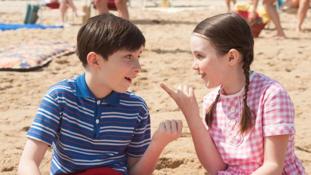 Ein Junge und ein Mädchen sitzen am Strand und unterhalten sich.