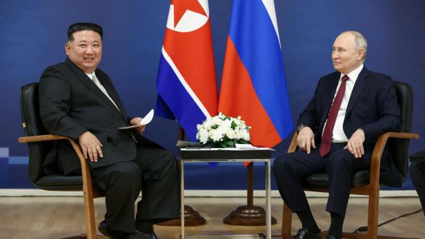 Putin und North Kim Jong-Un sitzen nebeneinander und lächeln