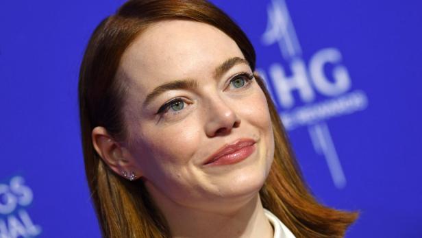 Emma Stone lächelt vor einem blauen Hintergrund.
