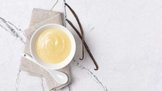 Eine Schale Vanillepudding mit Vanilleschoten auf einem Marmortisch.