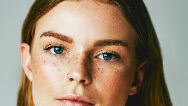 Porträt einer jungen Frau mit Sommersprossen und hellblauen Augen.