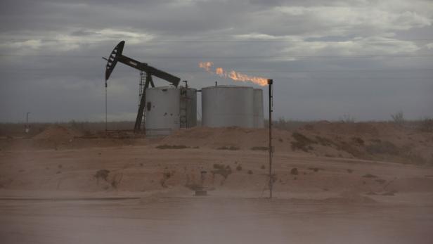 Eine brennende Gasfackel im Permianbecken, im Hintergrund eine Ölpumpe