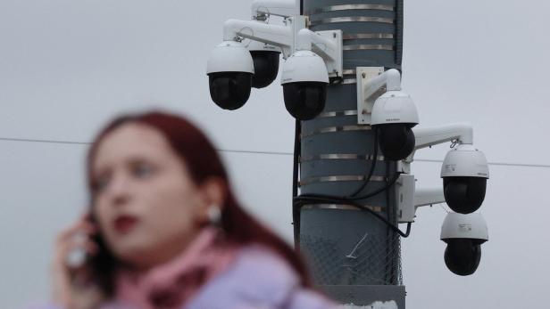 Symbolbild: Eine Frau mit telefoniert, im Hintergrund Überwachungskameras