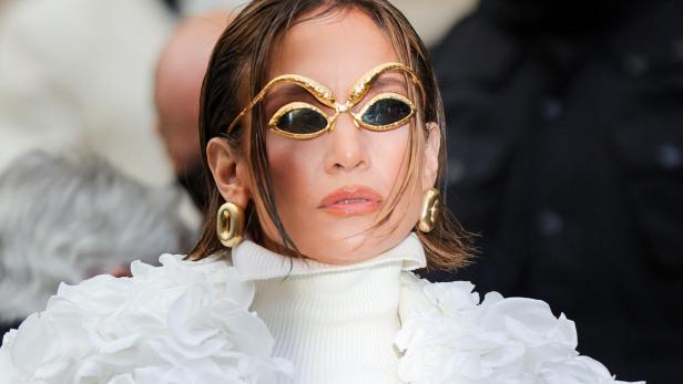 Jennifer Lopez trägt eine extravagante weiße Jacke und goldene Sonnenbrille.